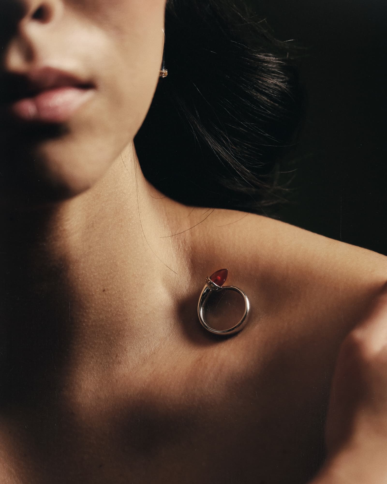 Close-up of a woman's neck with a silver ring pendant featuring a red gemstone.