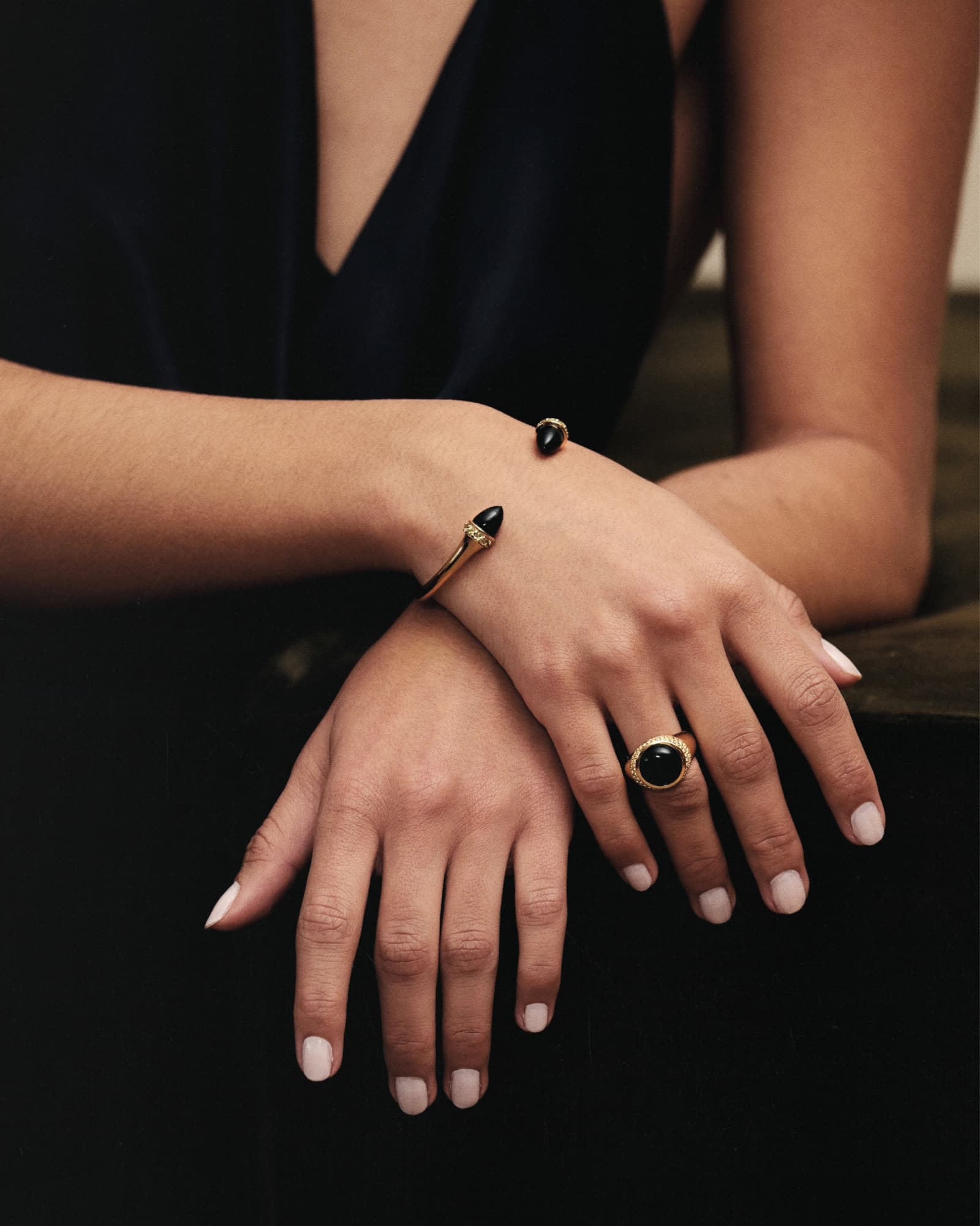 Close-up of a person's hands wearing a bracelet and ring with a black stone on a dark background