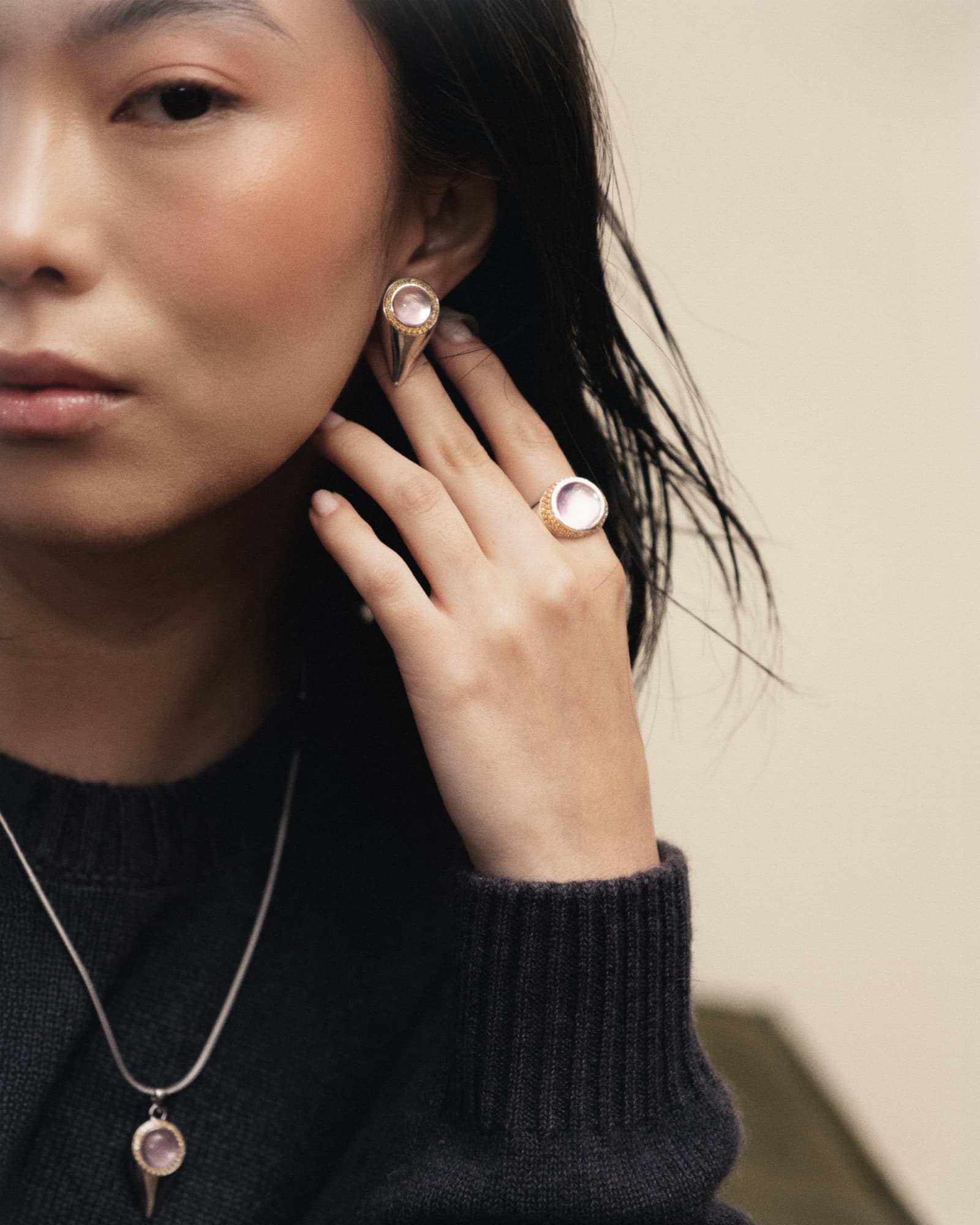 Woman wearing gold earrings and a ring with a visible brand logo.