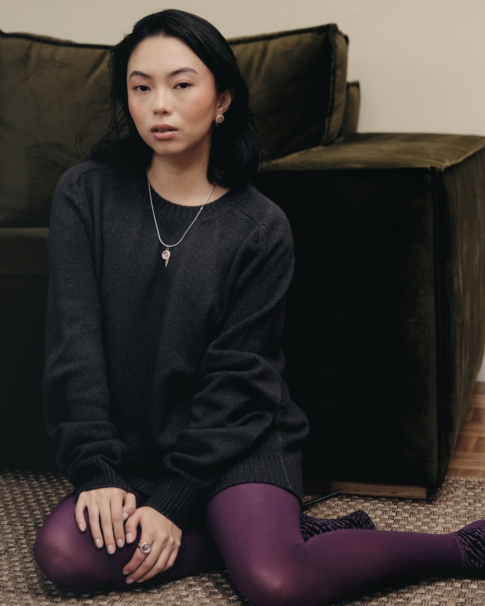 Woman sitting on the floor in a dark sweater and purple tights in a room with a brown couch.