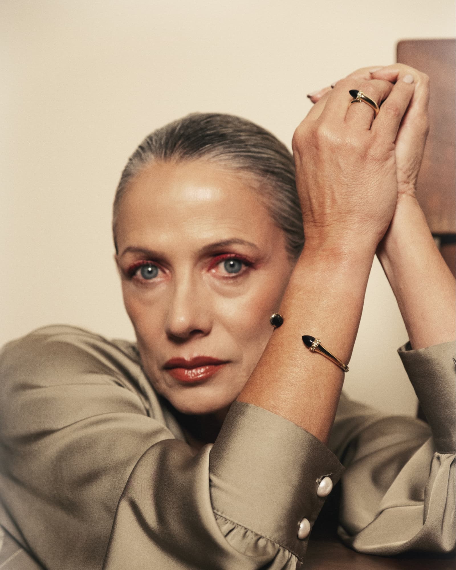 Woman with gray hair and jewelry, wearing a beige outfit against a neutral background