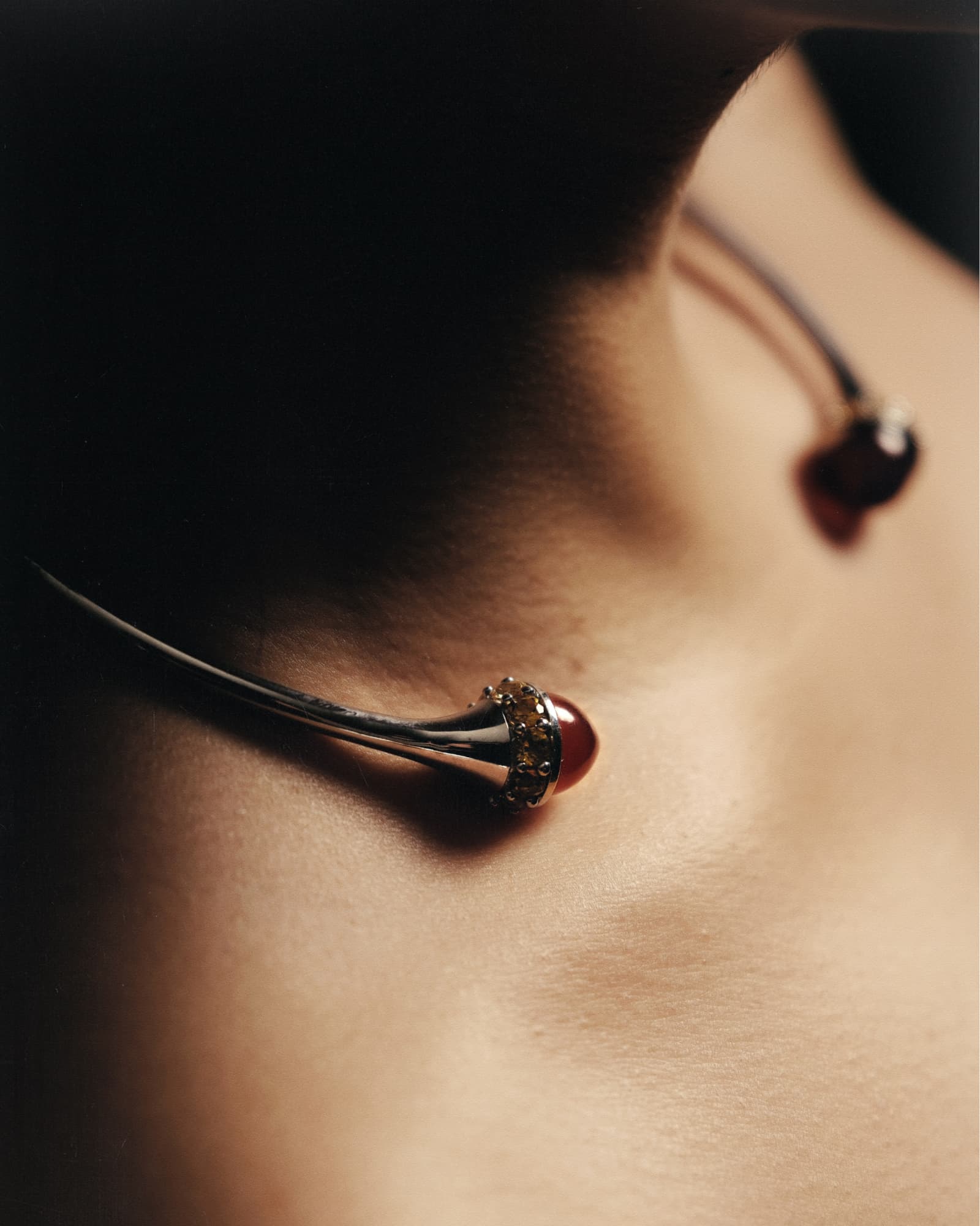 Close-up of a delicate necklace with a pendant on a person's neck against a dark background