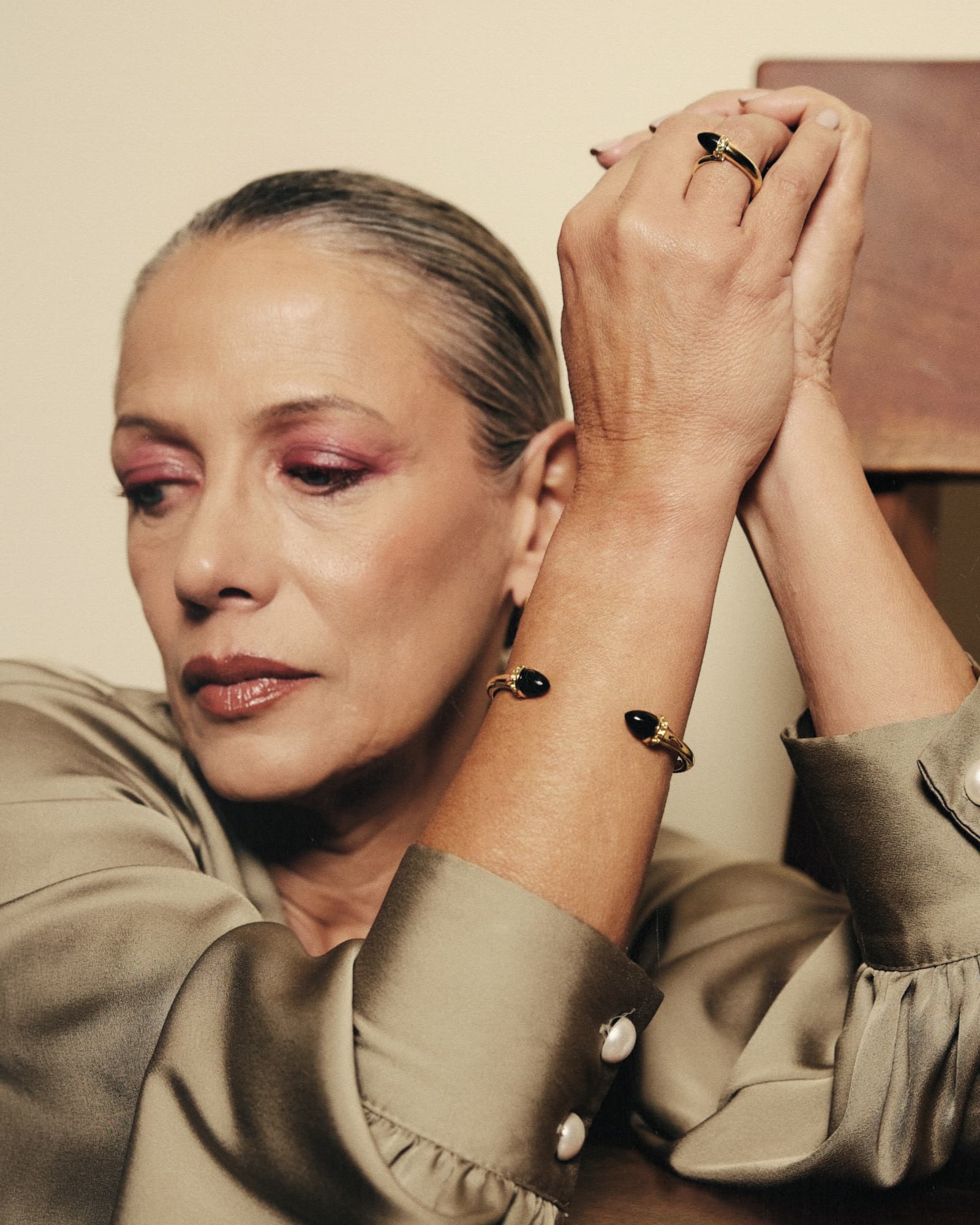 Woman with hands clasped, wearing jewelry, against a neutral background