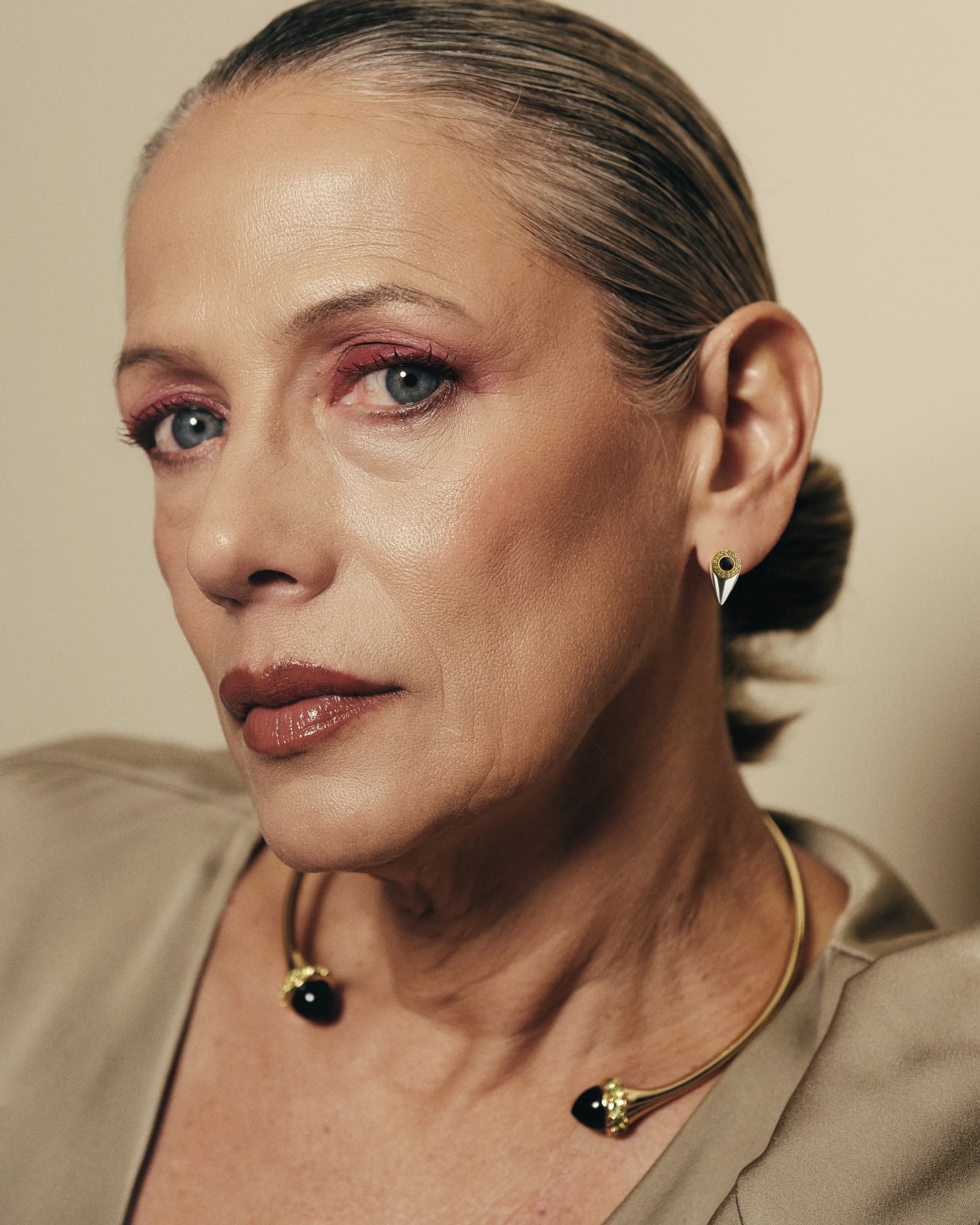 Close-up of a woman wearing gold earrings and necklace against a neutral background