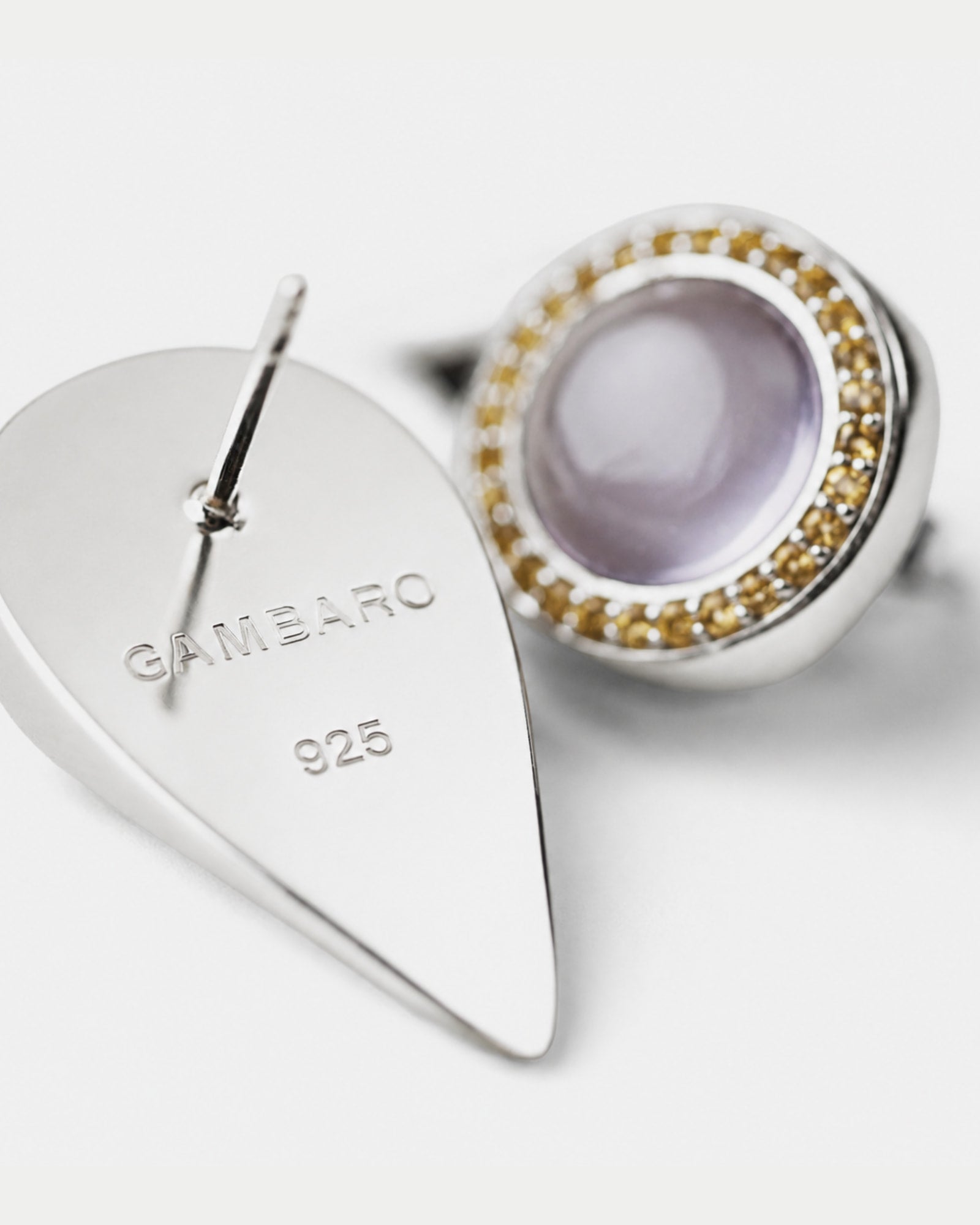 Silver teardrop-shaped stud earring with 'GAMBARO 925' engraved on the flat back, shown next to the front view featuring a round lavender-purple cabochon amethyst  stone surrounded by a halo of small gold citrine.